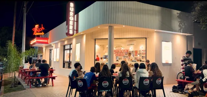 El local de Jesús María de noche, con gente comiendo en las mesas de picnic de la vereda